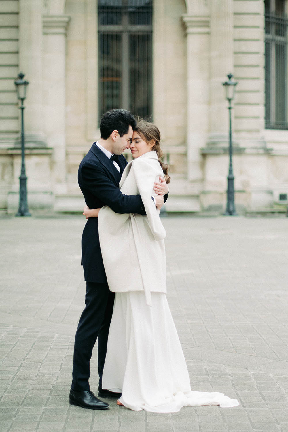 Des mariée se prennent dans les bras vers la pyramide du louvre